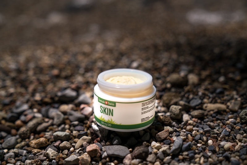 Ανοιχτό βάζο βαλσάμου CBD Skin της Formula Swiss, 300 mg CBD, σε παραλία με βότσαλα